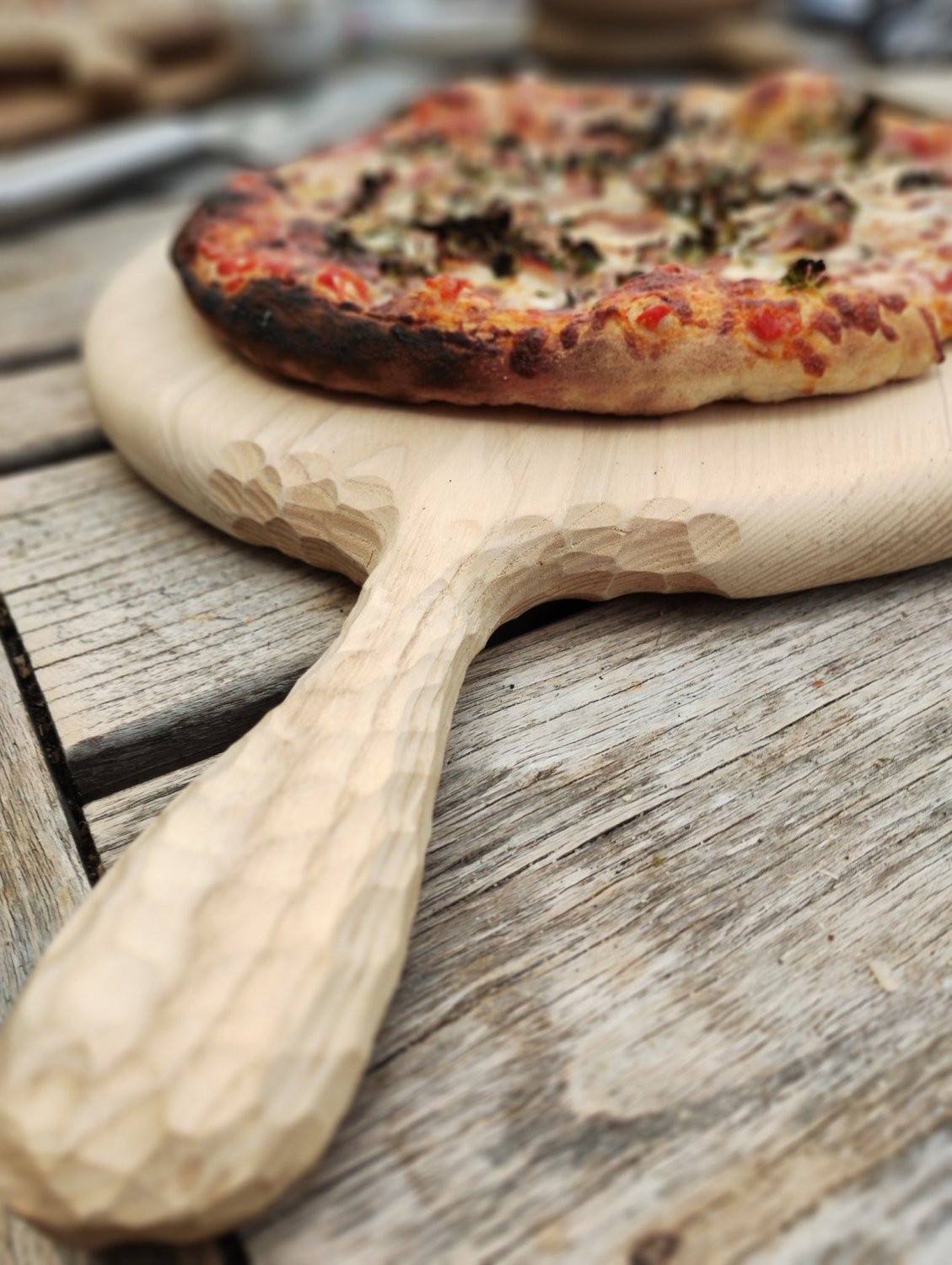 Round wooden pizza board with carved handle and a pizza on top