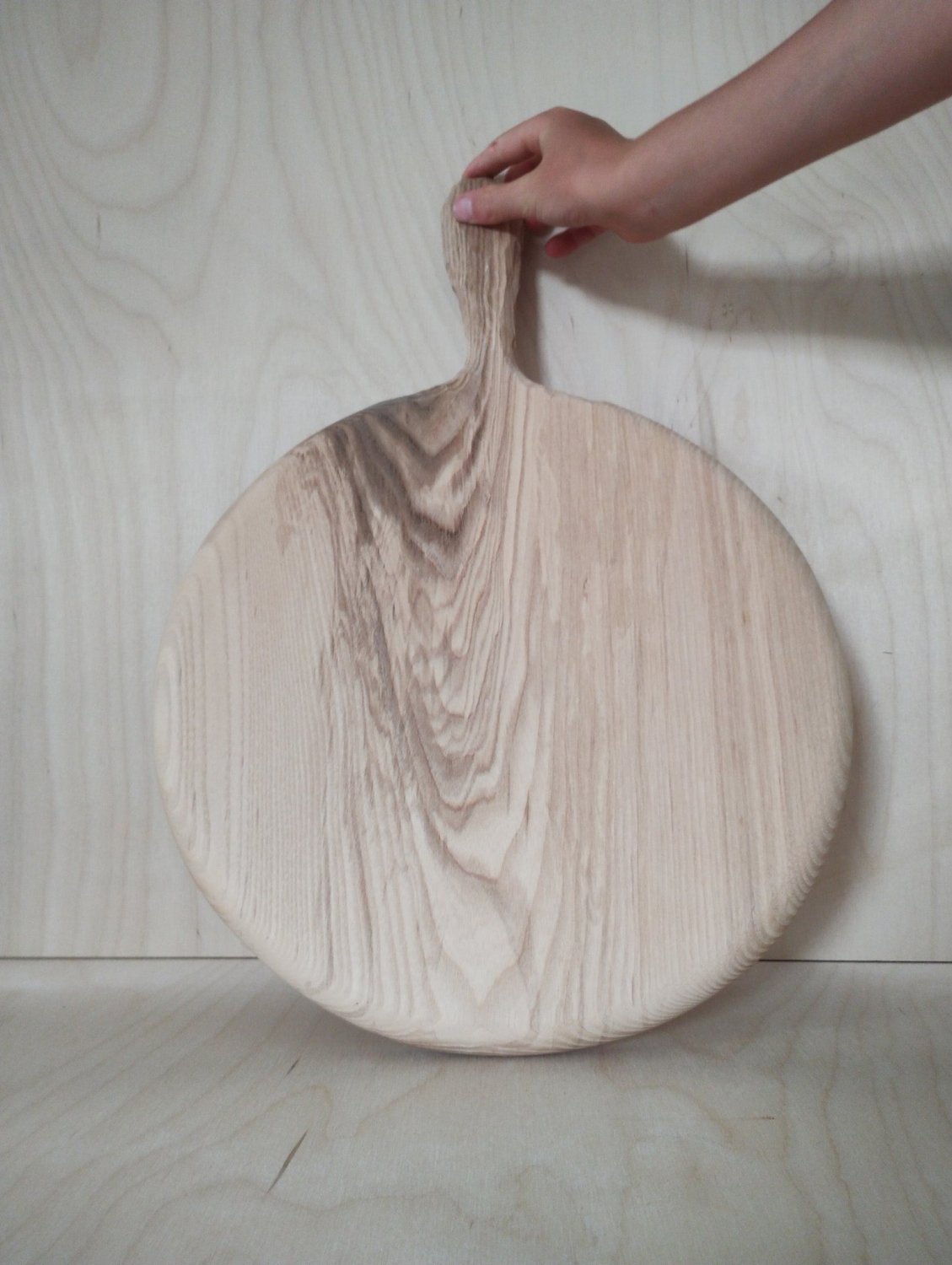 Round wooden pizza board with pedestal handle, grain patterns visible