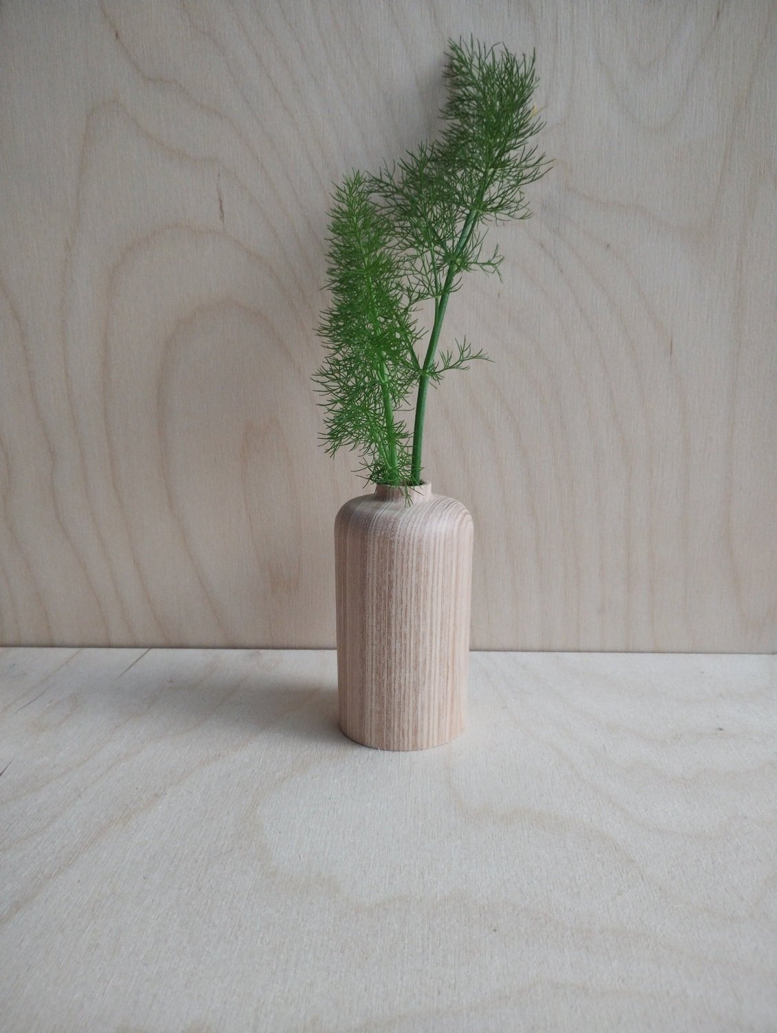 Small light-wood vase with vertical grain texture holding green plant sprig