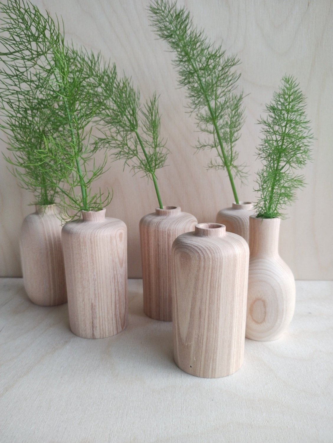 Collection of small vases with green stems, featuring light wood and white tones
