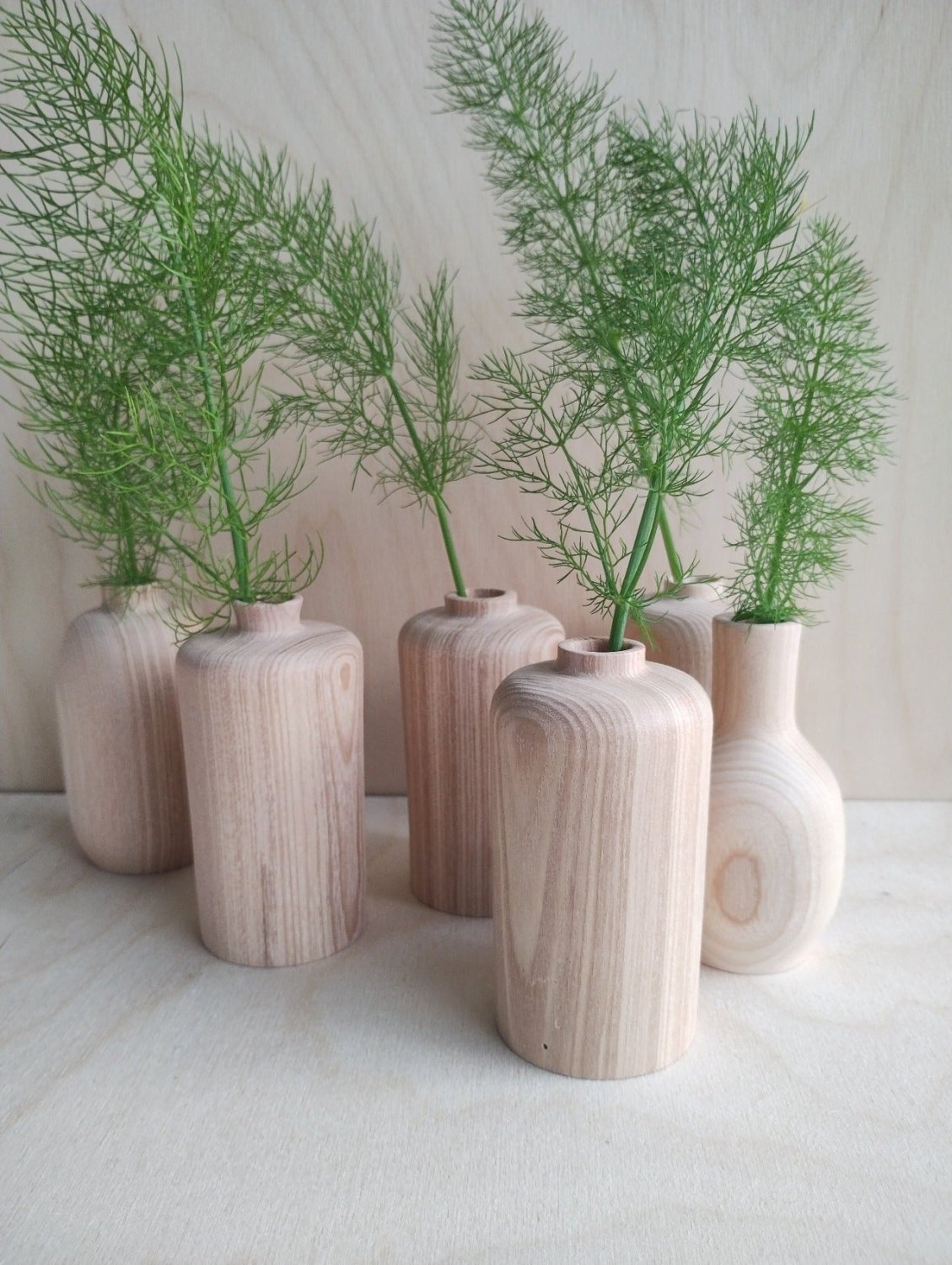 Small vases arranged together with green plant stems, light wood and white finishes