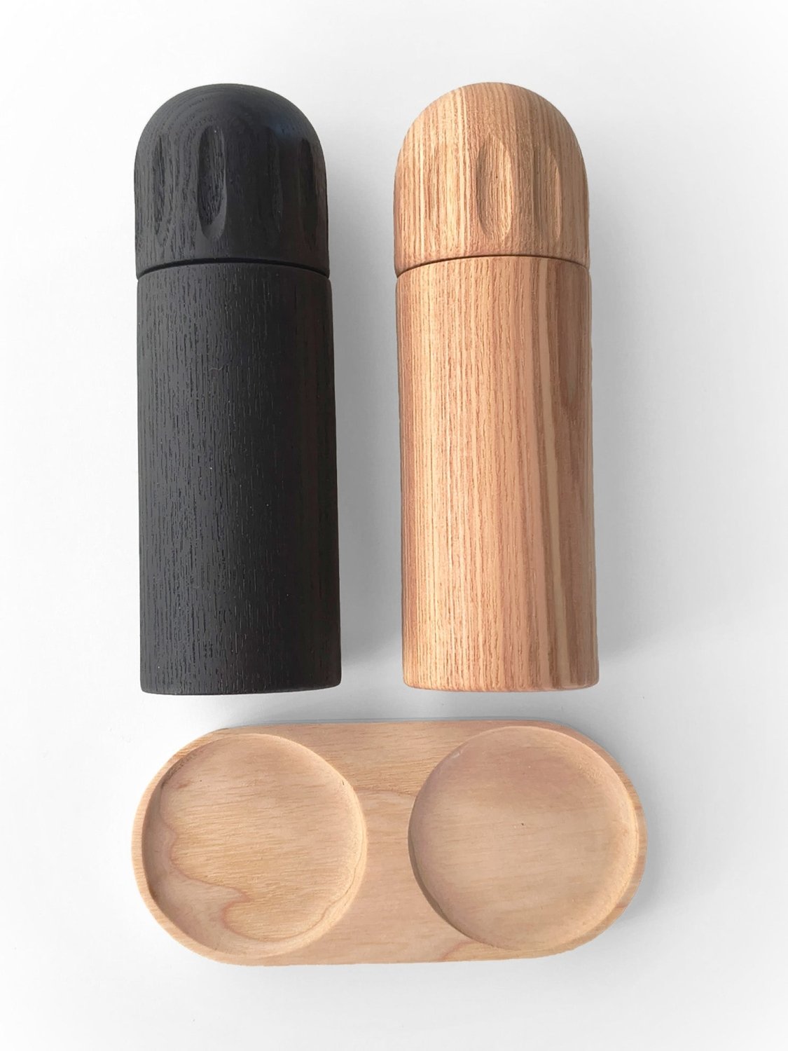 Two-piece set with dark and light wood pepper grinders and matching tray base