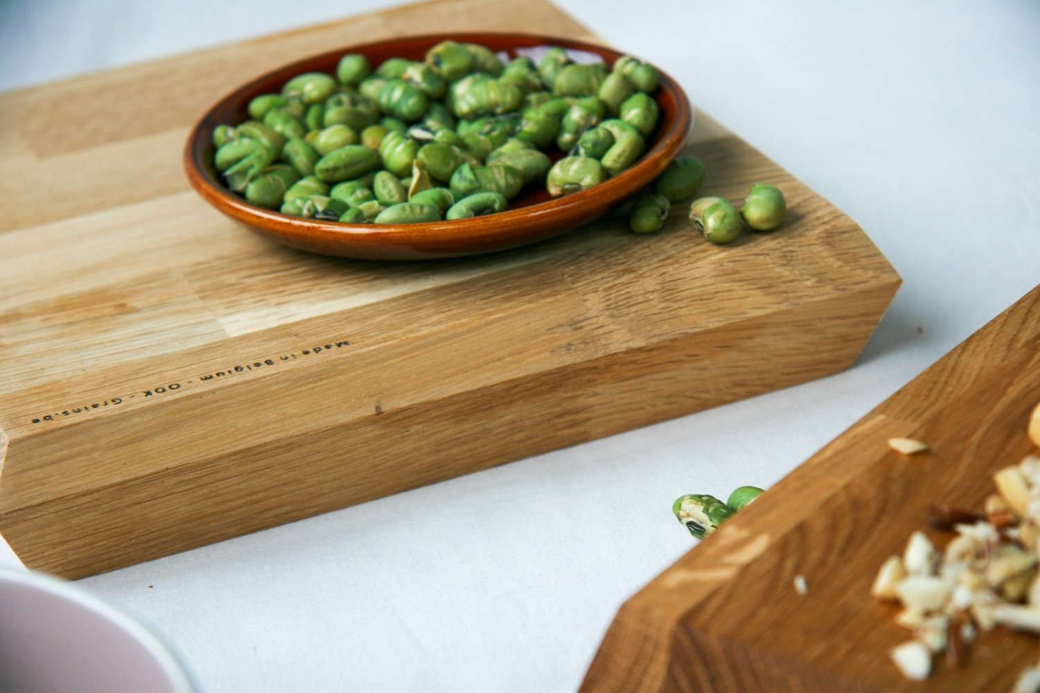 Wooden chopping board with a bowl of green peas and scattered chopped bits